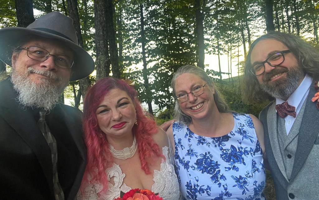 Two men and two women dressed for a wedding and smiling at the camera.