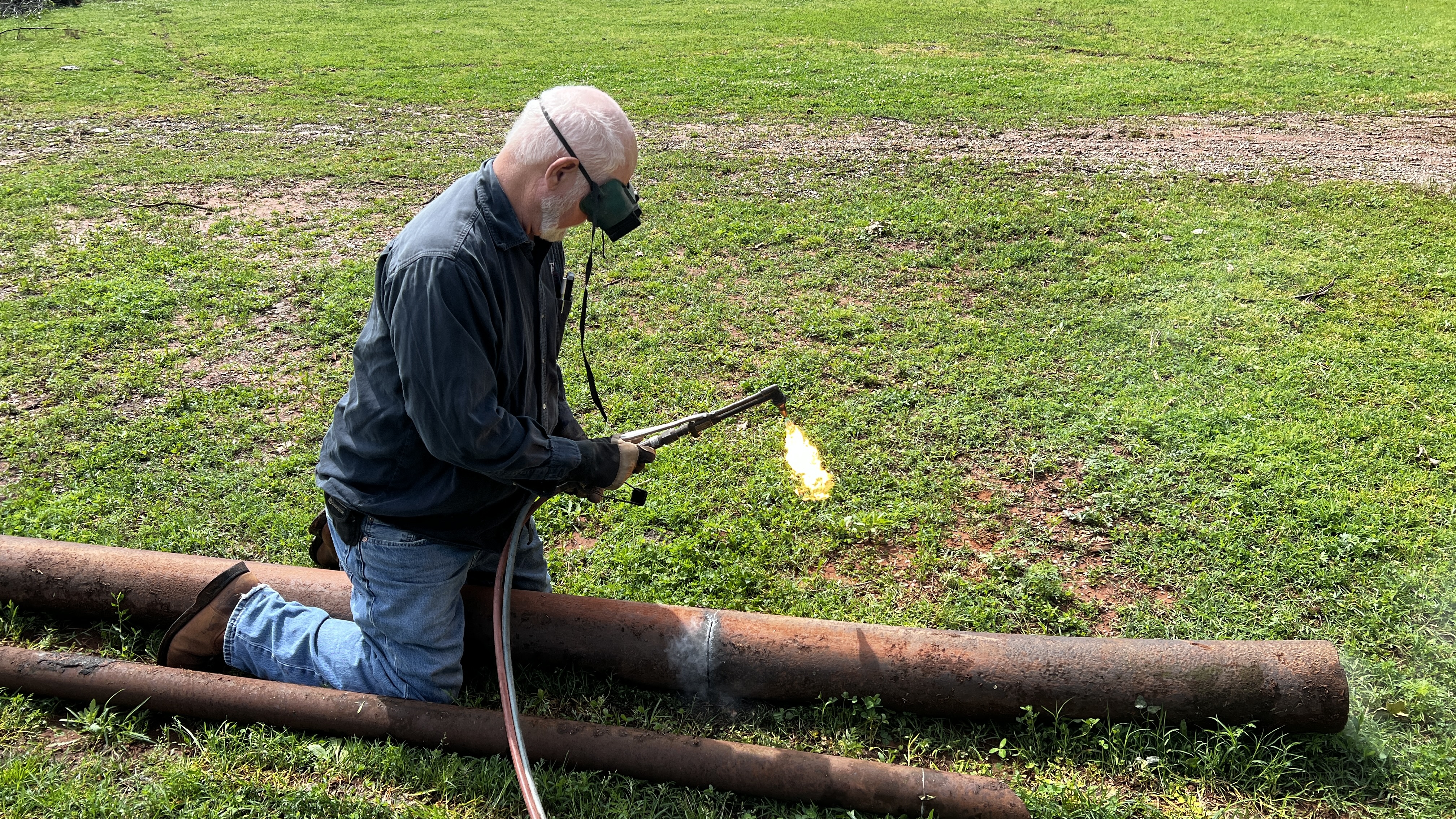A man with a cutting torch cutting a large pipe