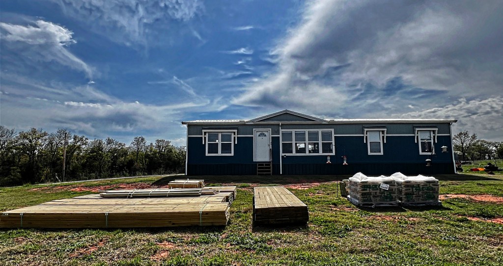 A manufactured home with lumber stacked in front.