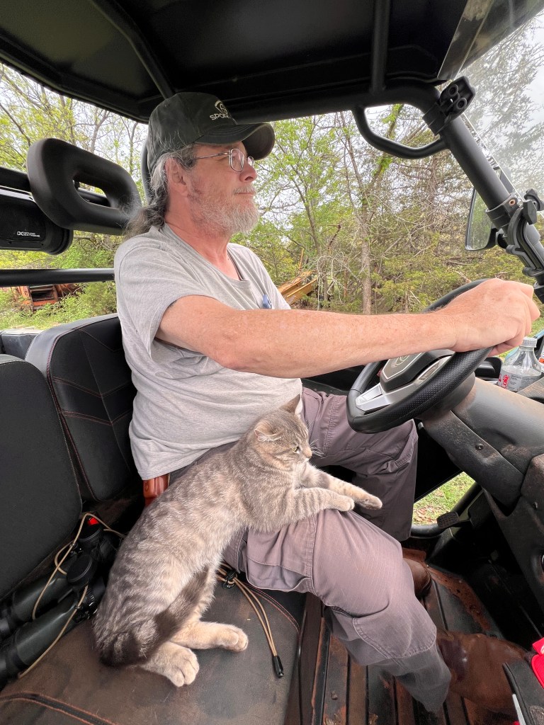 A man (me!) driving a UTV with a cat on his lap.